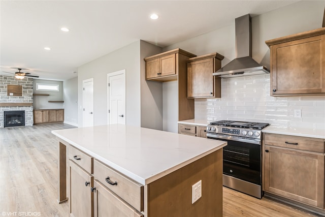 kitchen featuring ceiling fan, light wood-type flooring, gas range, a fireplace, and wall chimney exhaust hood