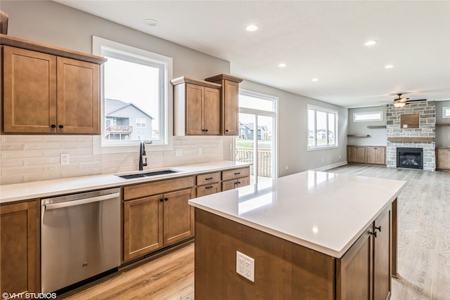 kitchen with backsplash, stainless steel dishwasher, sink, light wood-type flooring, and a stone fireplace