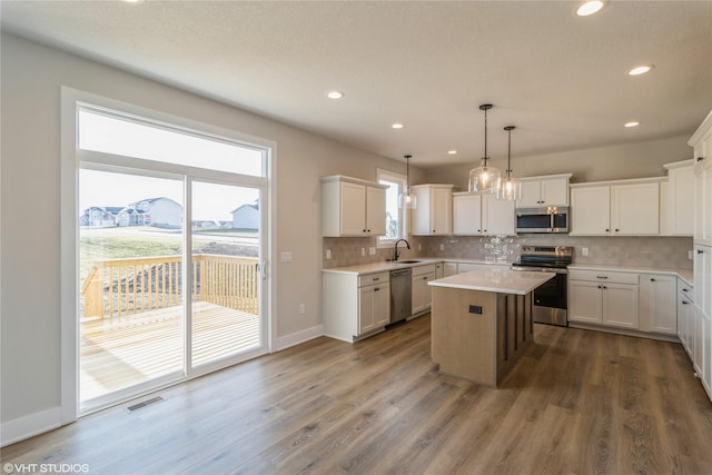 kitchen featuring a center island, white cabinetry, hanging light fixtures, appliances with stainless steel finishes, and dark wood-type flooring