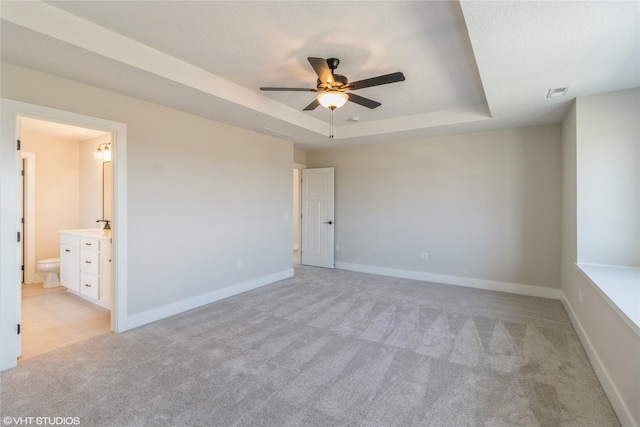 empty room with light carpet, ceiling fan, and a raised ceiling