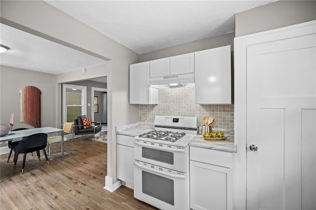 kitchen featuring tasteful backsplash, light hardwood / wood-style floors, white cabinetry, custom exhaust hood, and range with two ovens