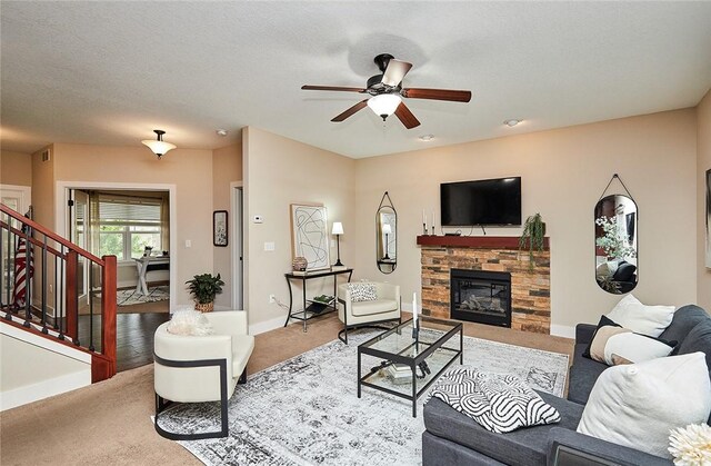 carpeted living room featuring a stone fireplace, a textured ceiling, and ceiling fan