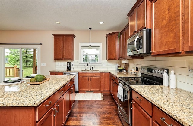 kitchen featuring stainless steel appliances, decorative light fixtures, light stone countertops, and sink