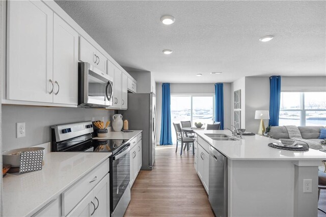 kitchen featuring appliances with stainless steel finishes, white cabinetry, an island with sink, sink, and light hardwood / wood-style floors