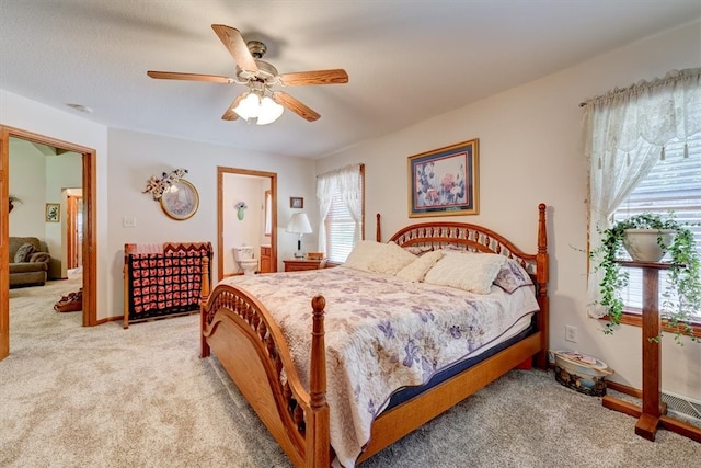 bedroom featuring ceiling fan, multiple windows, light colored carpet, and ensuite bathroom