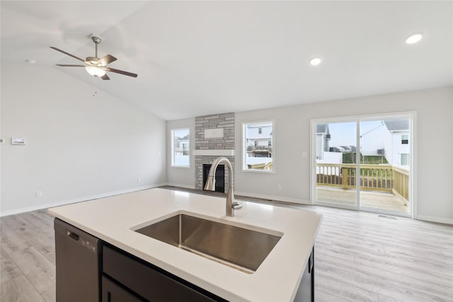 kitchen featuring sink, a center island with sink, light hardwood / wood-style flooring, dishwasher, and a fireplace