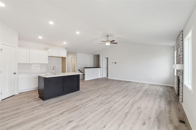 kitchen with sink, ceiling fan, tasteful backsplash, white cabinets, and a center island with sink