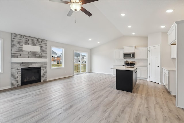 kitchen with a fireplace, white cabinetry, lofted ceiling, stainless steel appliances, and a center island with sink