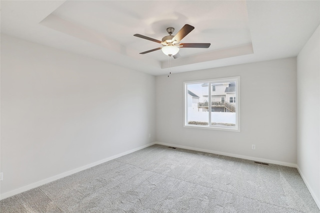 carpeted spare room featuring a raised ceiling and ceiling fan