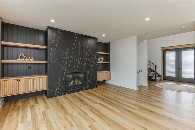 unfurnished living room with light wood-type flooring, french doors, a premium fireplace, and a textured ceiling