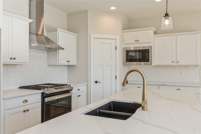 kitchen with sink, stainless steel gas range, wall chimney exhaust hood, white cabinetry, and black microwave