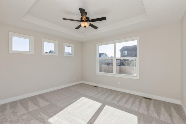 empty room with ceiling fan, light carpet, and a tray ceiling