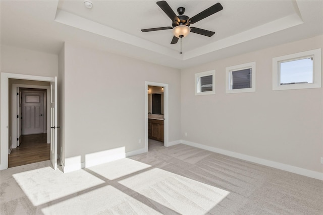 unfurnished bedroom featuring a raised ceiling, connected bathroom, ceiling fan, and light carpet