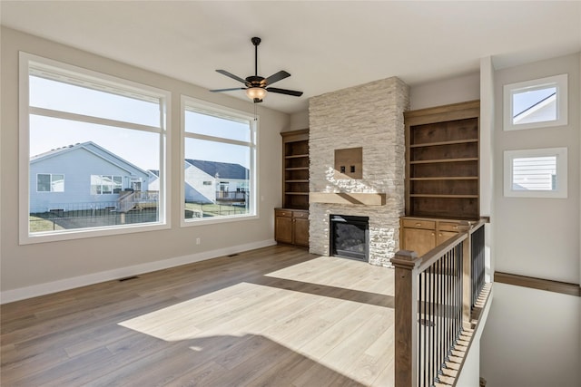 unfurnished living room with ceiling fan, a healthy amount of sunlight, a stone fireplace, and wood-type flooring