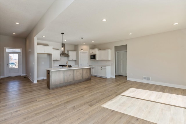 kitchen with a large island, white cabinets, wall chimney range hood, and light wood-type flooring