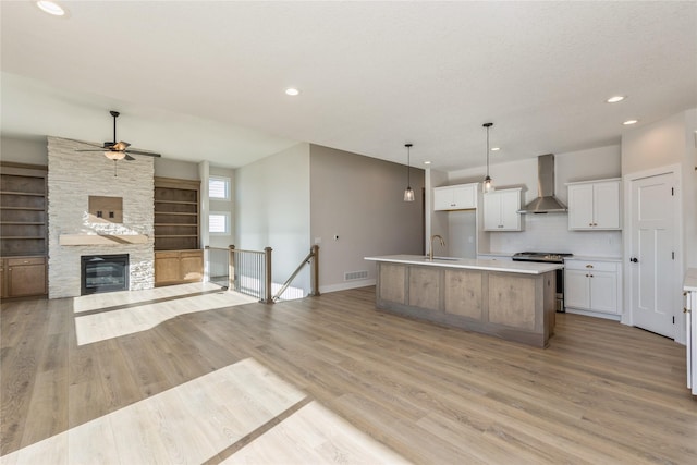 kitchen featuring stainless steel range, wall chimney range hood, a large island with sink, light hardwood / wood-style flooring, and white cabinets