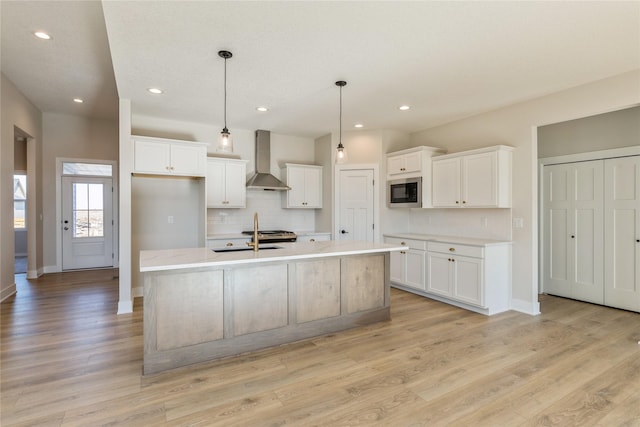 kitchen featuring pendant lighting, a center island with sink, sink, wall chimney exhaust hood, and white cabinetry