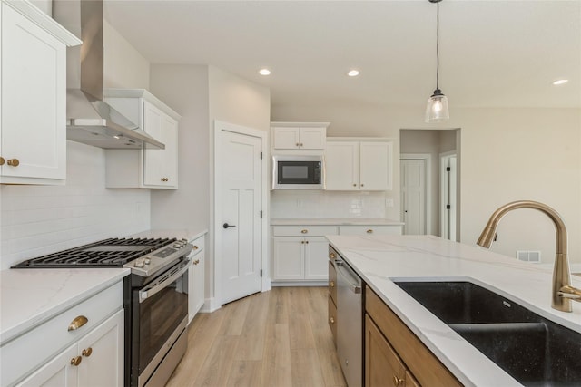 kitchen with white cabinetry, sink, light stone countertops, wall chimney range hood, and appliances with stainless steel finishes