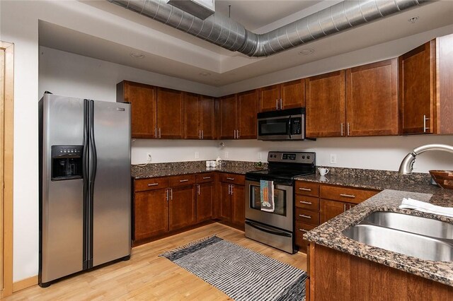 kitchen with appliances with stainless steel finishes, sink, light wood-type flooring, and dark stone countertops