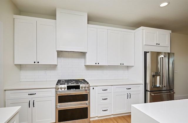 kitchen with light countertops, decorative backsplash, appliances with stainless steel finishes, white cabinets, and light wood-type flooring