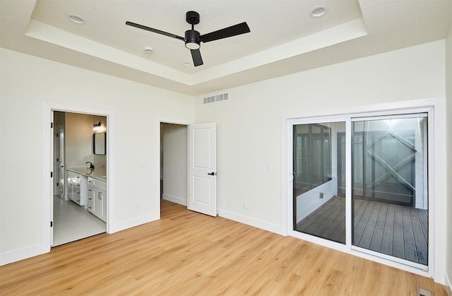 unfurnished bedroom with light wood-type flooring, visible vents, a tray ceiling, and access to outside