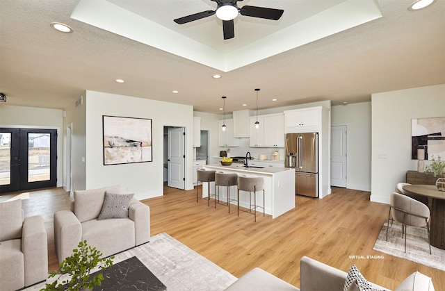 living room with light wood-type flooring, a raised ceiling, french doors, and recessed lighting