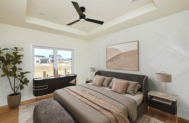 bedroom with ceiling fan, wood finished floors, a raised ceiling, and baseboards