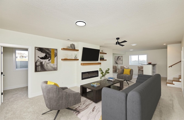 living room featuring a glass covered fireplace, light carpet, stairway, and a textured ceiling