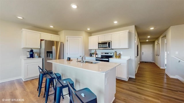 kitchen with sink, white cabinetry, light wood-type flooring, appliances with stainless steel finishes, and an island with sink