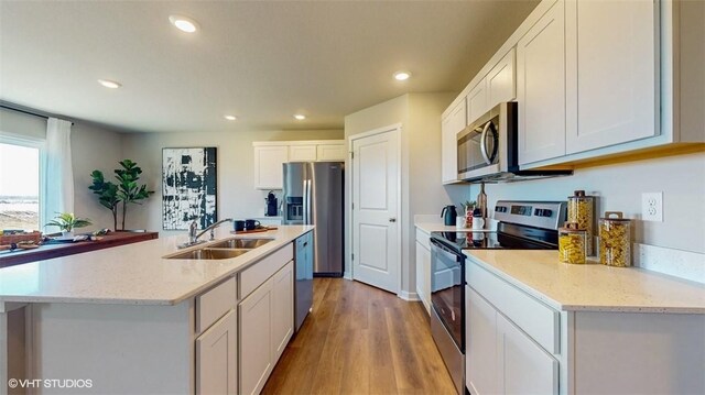 kitchen with sink, light wood-type flooring, stainless steel appliances, white cabinets, and a kitchen island with sink