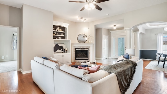 living room with a high end fireplace, wood-type flooring, decorative columns, built in features, and ceiling fan