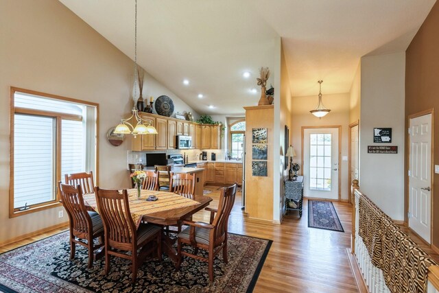 dining room featuring an inviting chandelier, light wood-type flooring, and high vaulted ceiling