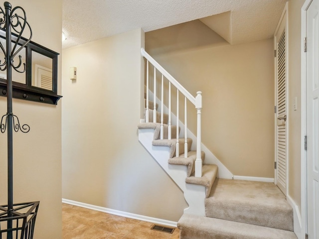 stairs featuring baseboards, visible vents, and a textured ceiling