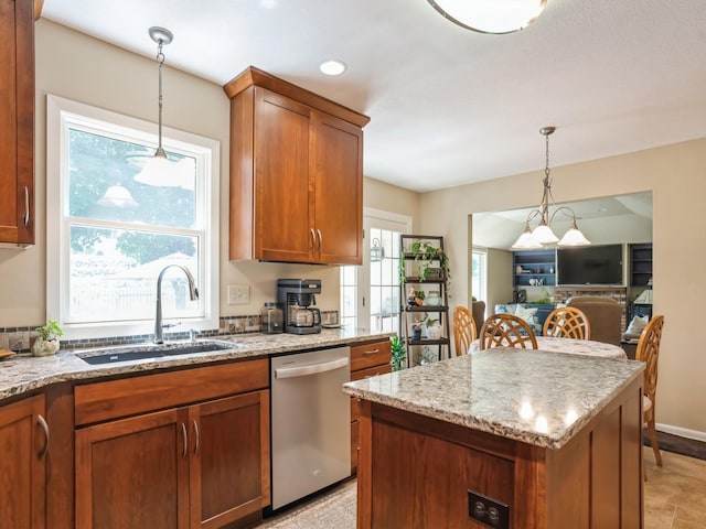 kitchen with pendant lighting, a sink, stainless steel dishwasher, brown cabinetry, and light stone countertops