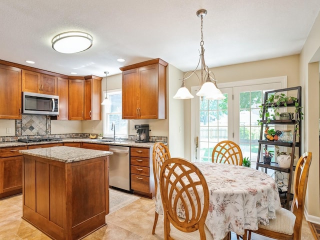 kitchen with light stone countertops, decorative backsplash, brown cabinets, appliances with stainless steel finishes, and a sink