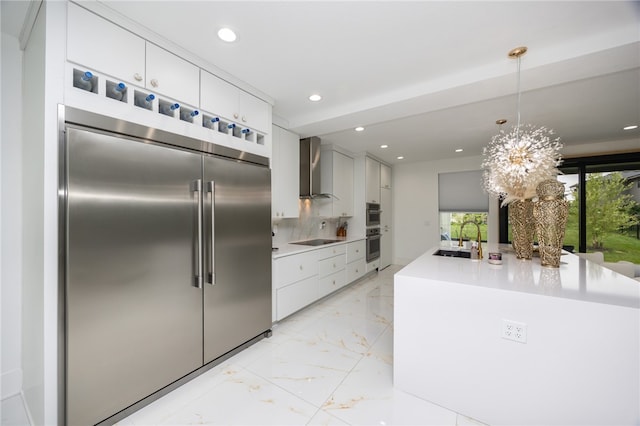 kitchen with sink, appliances with stainless steel finishes, decorative backsplash, wall chimney range hood, and white cabinets