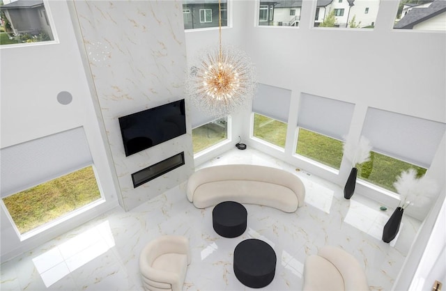 interior space featuring marble finish floor, a wealth of natural light, a notable chandelier, and a large fireplace