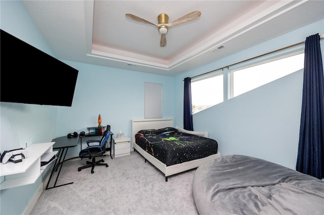 carpeted bedroom with a tray ceiling, visible vents, a ceiling fan, and baseboards