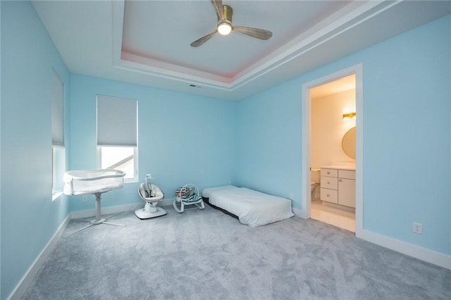 unfurnished bedroom with a tray ceiling, a ceiling fan, connected bathroom, baseboards, and carpet flooring