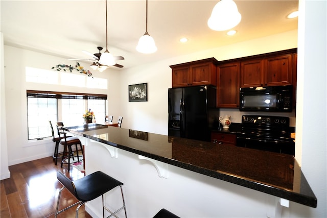 kitchen featuring ceiling fan, dark hardwood / wood-style flooring, hanging light fixtures, a breakfast bar area, and black appliances