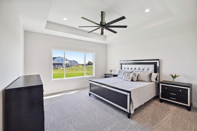 carpeted bedroom featuring ceiling fan and a raised ceiling