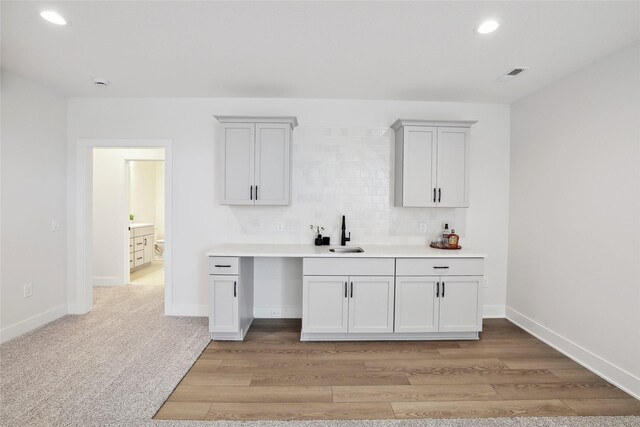 bar with light wood-type flooring, decorative backsplash, and sink