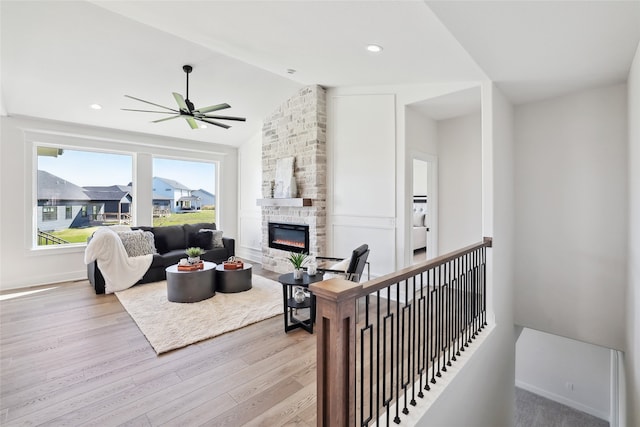 living room featuring light wood-type flooring, a fireplace, vaulted ceiling, and ceiling fan