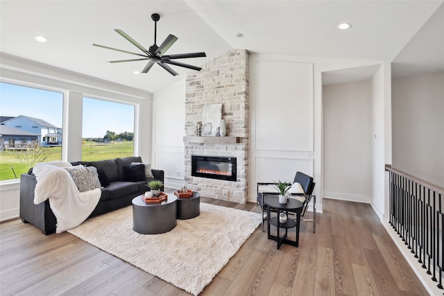 living room with light wood-type flooring, lofted ceiling, ceiling fan, and a fireplace