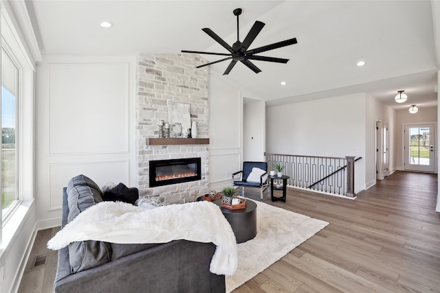 living room with lofted ceiling, ceiling fan, hardwood / wood-style flooring, and a stone fireplace