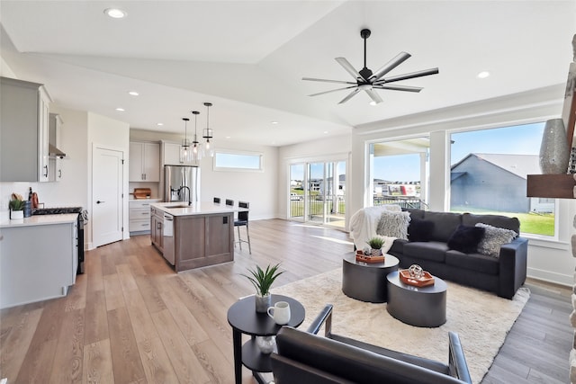 living room featuring light wood-type flooring, lofted ceiling, ceiling fan, and sink