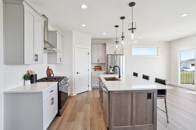 kitchen with light hardwood / wood-style floors, a kitchen island with sink, sink, hanging light fixtures, and appliances with stainless steel finishes