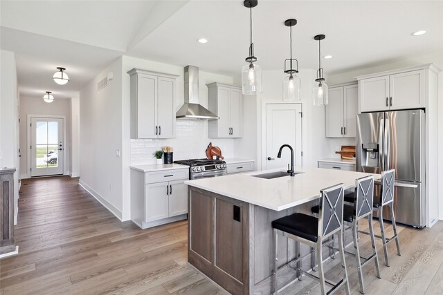 kitchen featuring hanging light fixtures, sink, wall chimney exhaust hood, stainless steel appliances, and light hardwood / wood-style floors