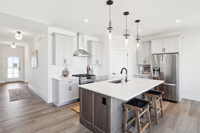 kitchen featuring a sink, light wood-style floors, appliances with stainless steel finishes, wall chimney exhaust hood, and tasteful backsplash