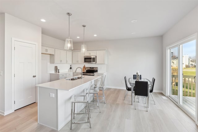 kitchen featuring appliances with stainless steel finishes, sink, a center island with sink, decorative light fixtures, and white cabinets